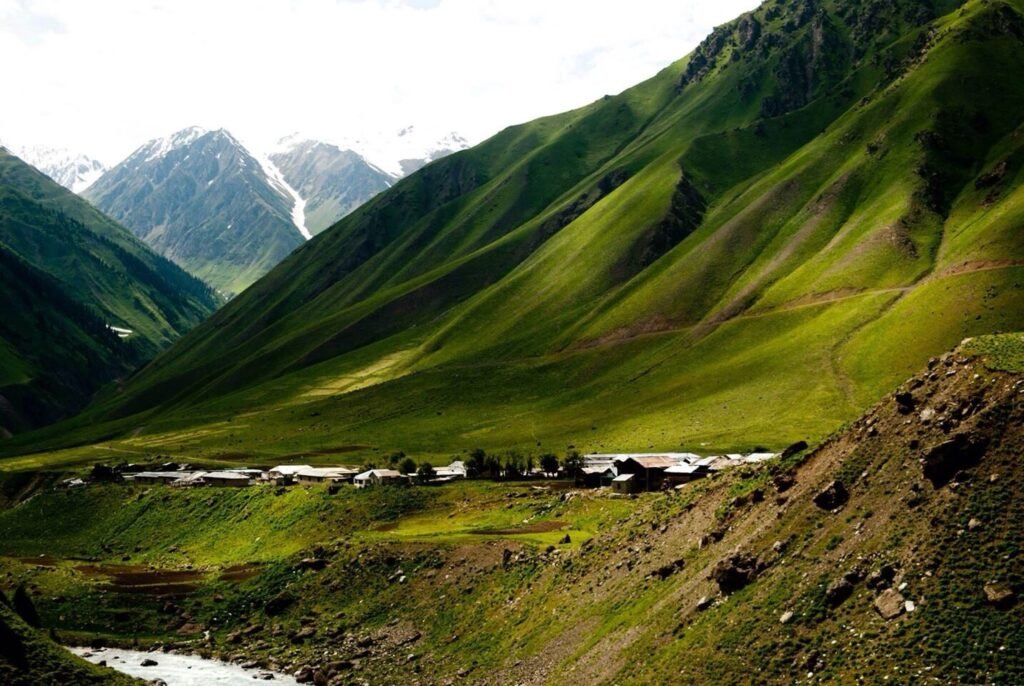 Breathtaking view of Minimarg in Kashmir with snow-capped mountains, lush green slopes, and a small village nestled in the valley