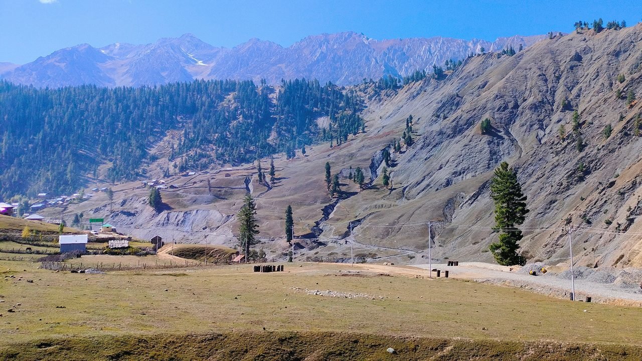 Panoramic view of Dawar village in Jammu and Kashmir with alpine meadows, pine-covered slopes, and rugged mountains in the background