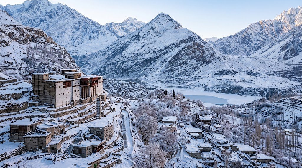 Snow-covered mountain peaks and a peaceful village nestled among the rugged landscapes of Hunza.