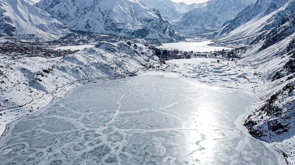 Frozen lake surrounded by snow-covered mountains and rugged winter scenery in Skardu.