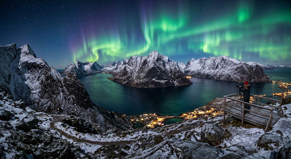 Alternative Text: Norway’s stunning fjords surrounded by snow-capped mountains beneath the colorful Northern Lights.